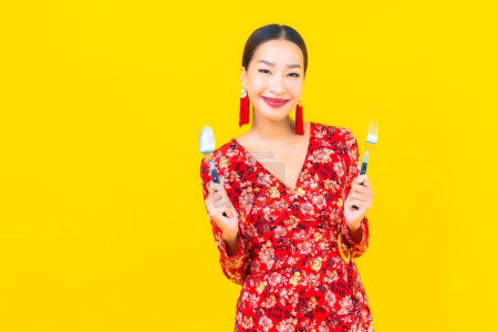 Téléchargez les photos : Portrait belle jeune femme asiatique avec cuillère et fourchette sur fond jaune - en image libre de droit