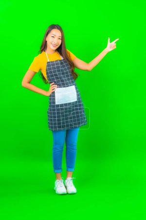 Photo for Portrait beautiful young asian woman wear apron with action on green isolated background - Royalty Free Image