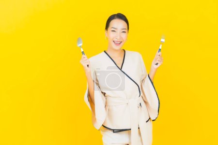 Téléchargez les photos : Portrait belle jeune femme asiatique d'affaires avec cuillère et fourchette prêt à manger de la nourriture sur fond jaune - en image libre de droit