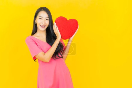 Foto de Retrato hermosa joven asiática mujer sonrisa con corazón almohada forma en color amarillo fondo - Imagen libre de derechos
