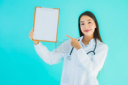 Foto de Retrato hermosa joven asiática médico mujer con tarjeta vacía cartel en azul aislado fondo - Imagen libre de derechos