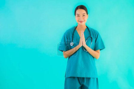 Téléchargez les photos : Portrait belle jeune asiatique médecin femme heureux sourire avec sawasdee pour le travail à l'hôpital et clinique sur fond bleu isolé - en image libre de droit