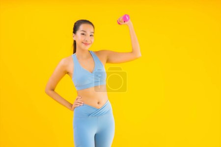 Téléchargez les photos : Portrait belle jeune femme asiatique avec haltère et vêtements de sport prêt pour l'exercice sur fond jaune isolé - en image libre de droit