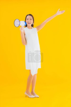 Téléchargez les photos : Portrait belle jeune femme asiatique avec mégaphone sur fond jaune isolé - en image libre de droit