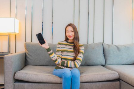 Foto de Retrato hermosa joven asiático mujer uso inteligente móvil en sofá en sala de estar interior - Imagen libre de derechos