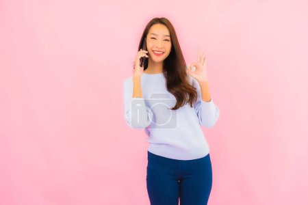 Téléchargez les photos : Portrait belle jeune femme asiatique utiliser téléphone mobile intelligent sur fond isolé couleur rose - en image libre de droit