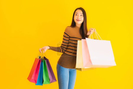 Téléchargez les photos : Portrait belle jeune femme asiatique sourire heureux avec beaucoup de couleur sac à provisions de grand magasin sur fond jaune isolé - en image libre de droit