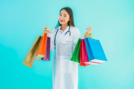 Téléchargez les photos : Portrait belle jeune femme médecin asiatique avec sac à provisions coloré du centre commercial sur fond bleu isolé - en image libre de droit