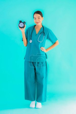 Foto de Portriat hermosa joven asiática médico mujer mostrar reloj o alarma en azul aislado fondo - Imagen libre de derechos