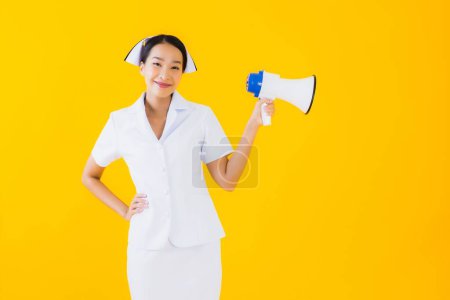 Foto de Retrato hermosa joven asiática mujer tailandesa enfermera con megáfono para comunicarse en la clínica y el hospital en amarillo aislado fondo - Imagen libre de derechos