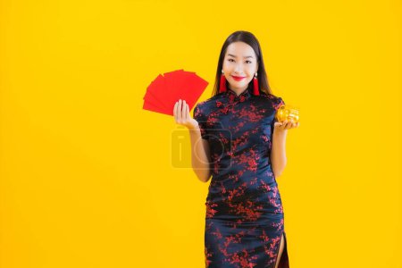 Photo for Portrait beautiful young asian woman wear chinese dress show gold piggy bank and red letter on yellow isolated background - Royalty Free Image