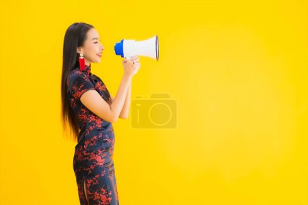 Téléchargez les photos : Portrait belle jeune femme asiatique porter robe chinoise avec mégaphone sur fond jaune isolé - en image libre de droit