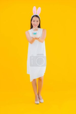 Téléchargez les photos : Portrait belle jeune femme asiatique avec oeuf de Pâques sur fond jaune isolé - en image libre de droit