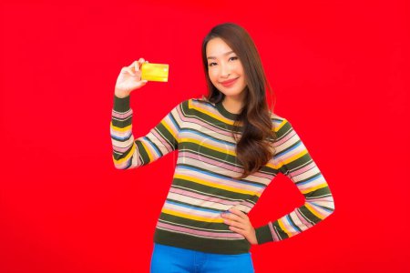 Téléchargez les photos : Portrait belle jeune femme asiatique avec carte de crédit sur fond rouge isolé - en image libre de droit