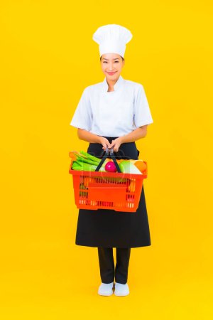 Photo for Portrait beautiful young asian chef woman with grocery basket from supermarket on yellow isolated background - Royalty Free Image