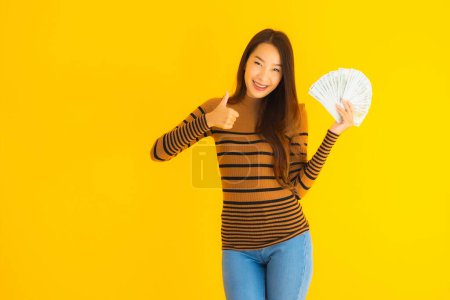Photo for Portrait beautiful young asian woman happy smile and rich with a lot of cash in her hand on yellow isolated background - Royalty Free Image