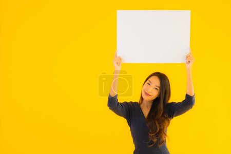Foto de Retrato hermosa joven asiática mujer con vacío y en blanco cartel de la tarjeta de banner en amarillo aislado fondo - Imagen libre de derechos