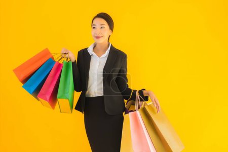 Téléchargez les photos : Portrait belle jeune femme asiatique d'affaires avec sac à provisions de centre commercial sur fond jaune isolé - en image libre de droit