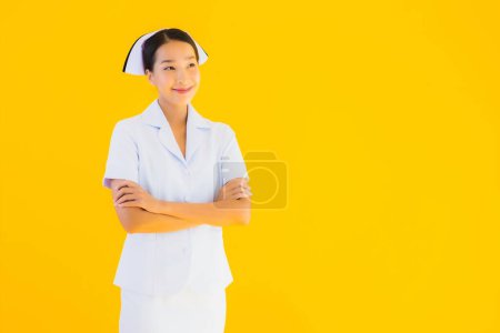 Foto de Retrato hermoso joven asiático tailandés enfermera en muchos trabajo de acción para el paciente en la clínica y el hospital en amarillo aislado fondo - Imagen libre de derechos