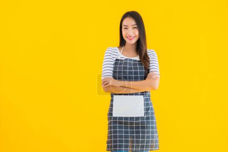 Photo for Portrait beautiful young asian woman wear apron with smile happy on yellow isolated background - Royalty Free Image