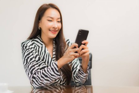 Téléchargez les photos : Portrait belle jeune femme asiatique utiliser ordinateur portable avec téléphone portable intelligent sur la table de travail dans la chambre - en image libre de droit
