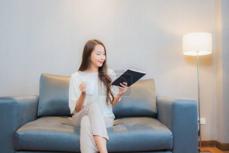 Téléchargez les photos : Portrait belle jeune femme asiatique lire le livre sur canapé dans le salon intérieur - en image libre de droit