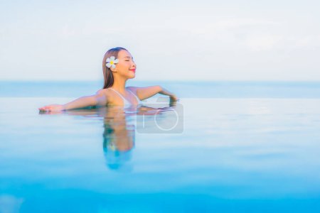 Téléchargez les photos : Portrait belle jeune femme asiatique se détendre sourire autour de la piscine extérieure dans hôtel station balnéaire presque mer plage océan - en image libre de droit