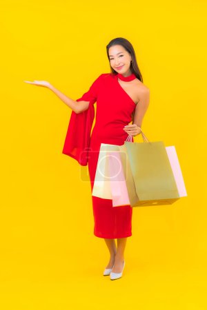 Téléchargez les photos : Portrait belle jeune femme asiatique avec sac à provisions et carte de crédit sur fond jaune - en image libre de droit