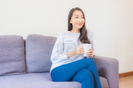 Téléchargez les photos : Portrait belle jeune femme asiatique avec tasse de café sur canapé dans le salon intérieur - en image libre de droit