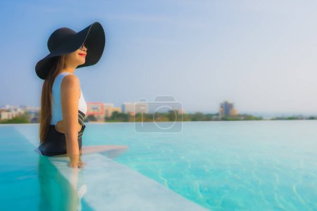 Téléchargez les photos : Portrait belle jeune femme asiatique sourire heureux se détendre autour de la piscine extérieure dans la station hôtelière pour des vacances de voyage - en image libre de droit