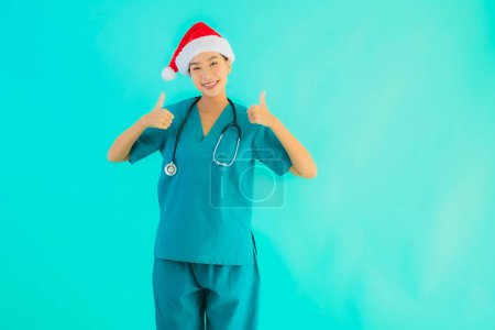 Téléchargez les photos : Portrait belle jeune asiatique médecin femme porter chapeau de Noël avec sourire heureux sur fond bleu isolé - en image libre de droit