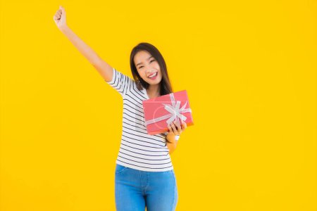 Foto de Retrato hermosa joven asiática mujer mostrar rojo caja de regalo en amarillo aislado fondo - Imagen libre de derechos