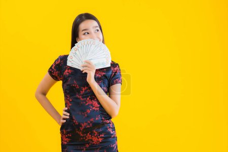 Foto de Retrato hermosa mujer asiática joven usar vestido chino con un montón de dinero en efectivo o dinero para el concepto de año nuevo chino sobre fondo aislado amarillo - Imagen libre de derechos