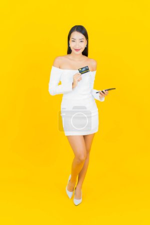 Foto de Retrato hermosa joven mujer asiática de negocios con teléfono móvil inteligente y tarjeta de crédito sobre fondo amarillo - Imagen libre de derechos