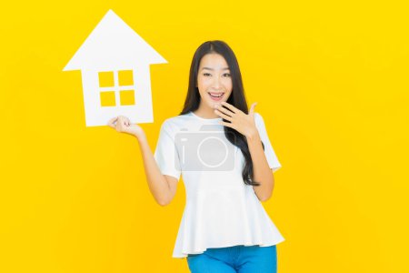 Foto de Retrato hermosa joven mujer asiática con casa o casa cartel de papel sobre fondo de color amarillo - Imagen libre de derechos