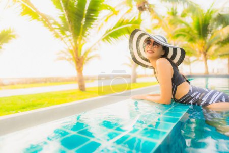 Foto de Retrato hermosa mujer asiática joven relajarse alrededor de la piscina al aire libre en el complejo hotelero con palmera al atardecer o al amanecer para vacaciones de ocio - Imagen libre de derechos