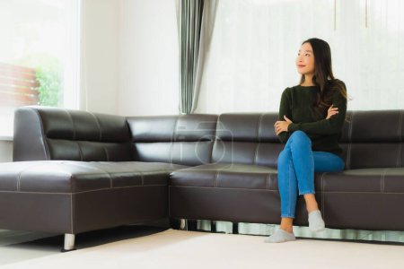 Foto de Hermoso retrato joven asiático mujer sentarse relajarse en sofá en sala de estar interior - Imagen libre de derechos