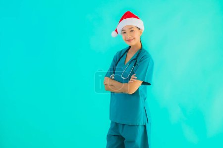 Foto de Retrato hermosa joven asiática médico mujer usar navidad sombrero con sonrisa feliz en azul aislado fondo - Imagen libre de derechos