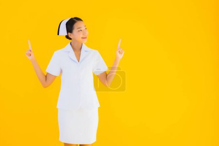 Téléchargez les photos : Portrait belle jeune infirmière asiatique thai dans beaucoup de travail d'action pour le patient en clinique et à l'hôpital sur fond jaune isolé - en image libre de droit