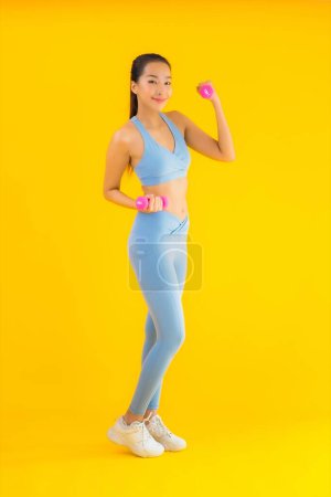 Foto de Retrato hermosa joven asiática mujer con mancuerna y ropa deportiva listo para el ejercicio en amarillo aislado fondo - Imagen libre de derechos