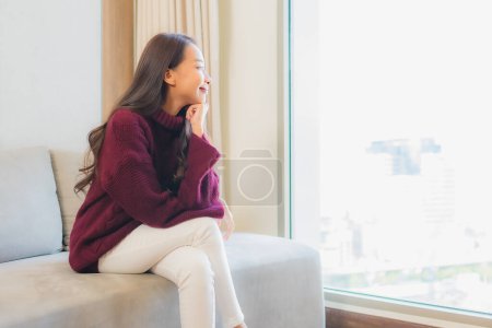 Téléchargez les photos : Portrait belle jeune femme asiatique sourire se détendre sur canapé dans le salon intérieur - en image libre de droit