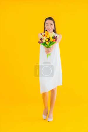 Téléchargez les photos : Portrait belle jeune femme asiatique avec fleur sur fond jaune isolé - en image libre de droit