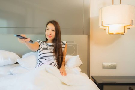 Photo for Portrait beautiful young asian woman use remote tv on bed in bedroom interior - Royalty Free Image