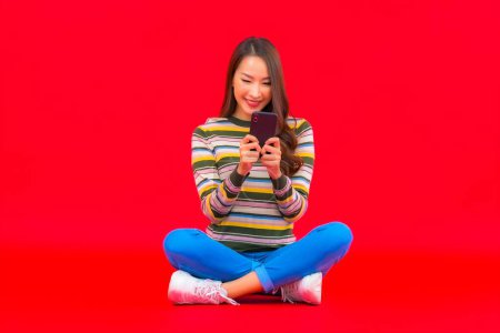 Foto de Retrato hermosa joven asiática mujer uso inteligente móvil en rojo aislado fondo - Imagen libre de derechos
