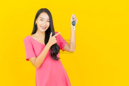 Téléchargez les photos : Portrait belle jeune femme asiatique sourire avec clé de voiture sur fond de couleur jaune - en image libre de droit