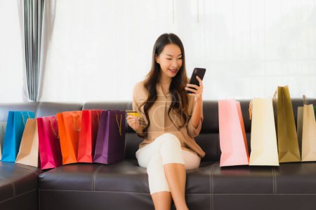 Photo for Portrait beautiful young asian woman online shopping with credit card and smartphone around shopping bag in living room - Royalty Free Image