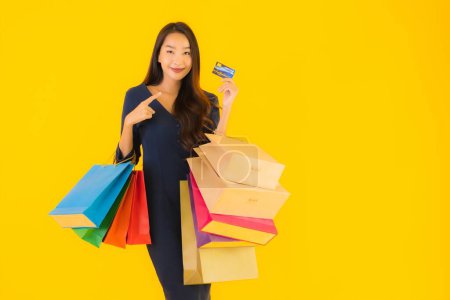 Foto de Retrato hermosa joven asiática mujer con bolsa de compras tarjeta de crédito y teléfono móvil inteligente amarillo aislado fondo - Imagen libre de derechos