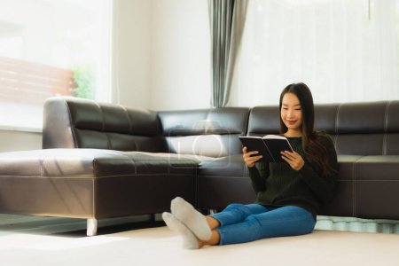 Téléchargez les photos : Portrait belle jeune femme asiatique lire livre avec tasse de café et canapé dans le salon intérieur - en image libre de droit