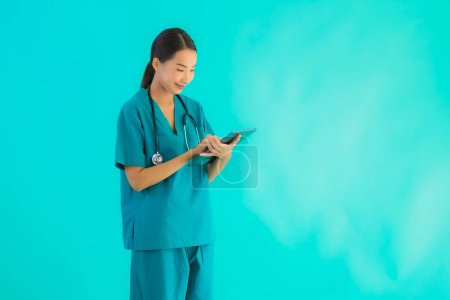 Téléchargez les photos : Portrait belle jeune asiatique médecin femme utiliser appareil tablette intelligente sur fond bleu isolé - en image libre de droit