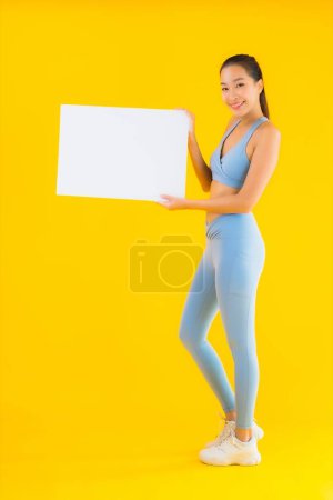 Foto de Retrato hermosa joven mujer asiática desgaste ropa deportiva espectáculo cartelera blanca vacía en amarillo aislado fondo - Imagen libre de derechos